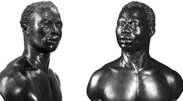 Photograph. Two carved, black stone busts include the heads, necks, and chests of almost identical Black men. Both have short, curly hair, noticeable eyebrow ridges, wide noses, and their full lips are closed. Tendons stand out in their necks, which turn halfway to profile. They have muscular shoulders and chests. One is angled to look off to our right, and the other to our left.