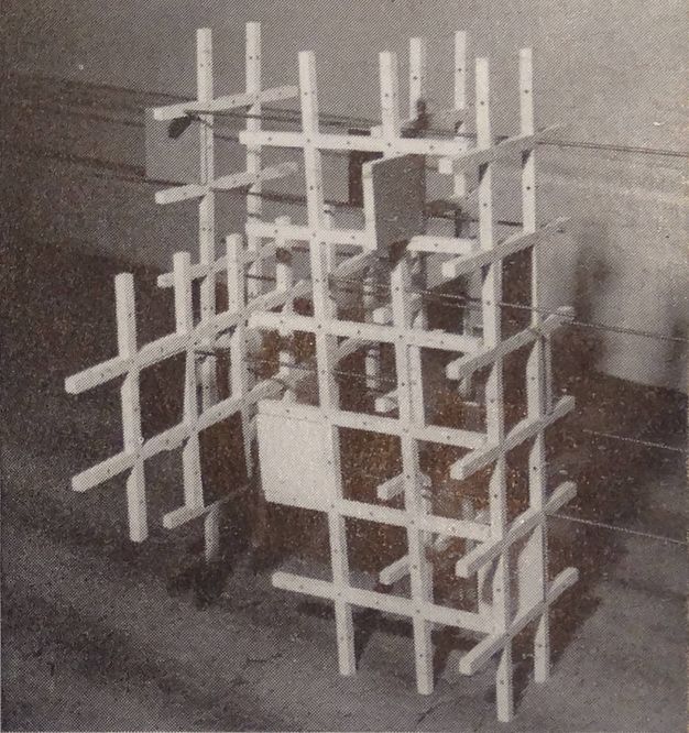 Sculpture. This grainy black and white photograph shows six long lattices built into an irregular, tower-like structure. Long rods through holes drilled in the beams hold the work together.