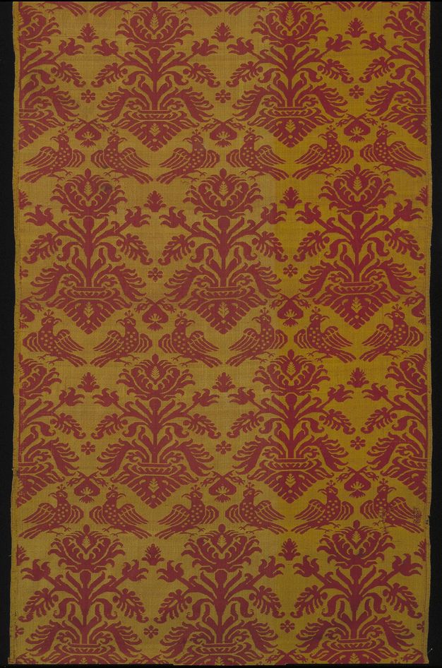 Textile. Stylized birds and flowers create a pattern in maroon red against a muted gold background.