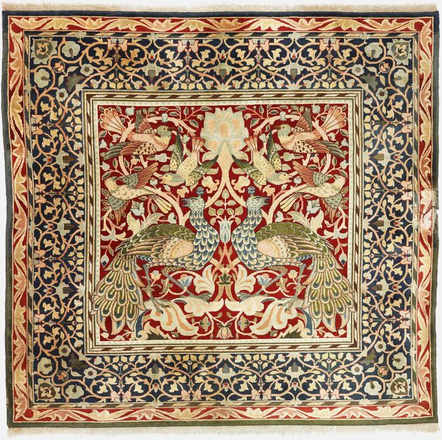 Carpet. A dense pattern created in tones of ruby red, sage green, muted blue, shell pink, and cream white shows two peacocks and six birds in a central panel surrounded by a wide band of leafy vines.