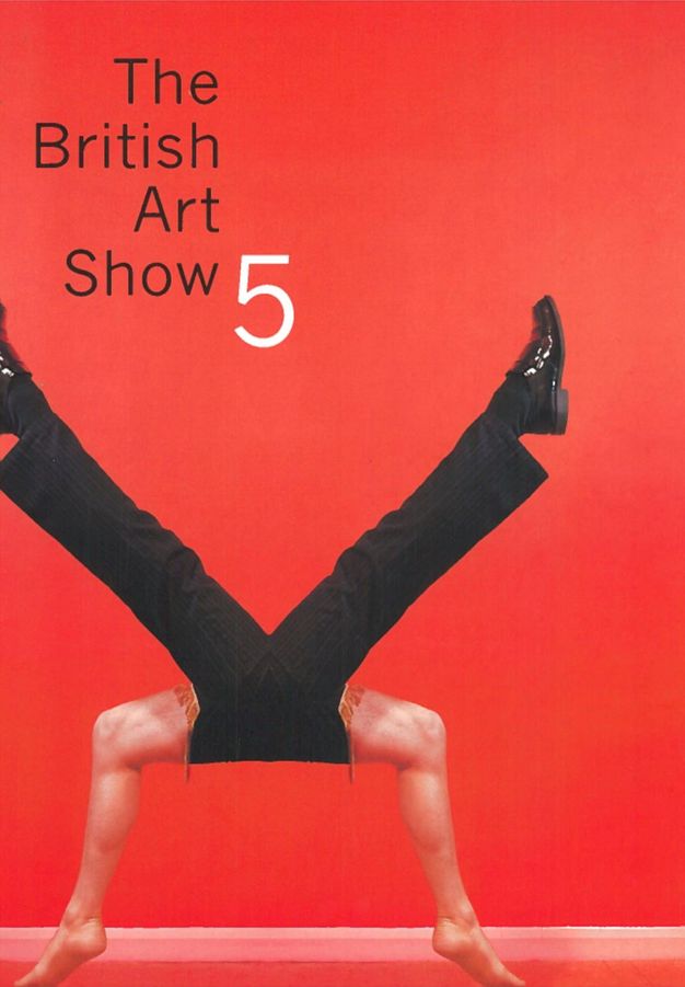 Cover of an exhibition catalogue. Against a scarlet-red background, two pairs of legs are incongruously joined where the hips might be to create a rough X shape. The pair of legs on top wear black, pinstripe slacks and shiny patent leather shoes. The other pair of pale-skinned legs are bare. 